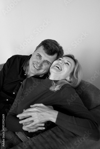 attractive middle-aged married couple hugging and smiling on sofa, studio photo shoot