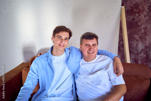    a  portrait of a middle-aged man  and his adult son sitting on sofa