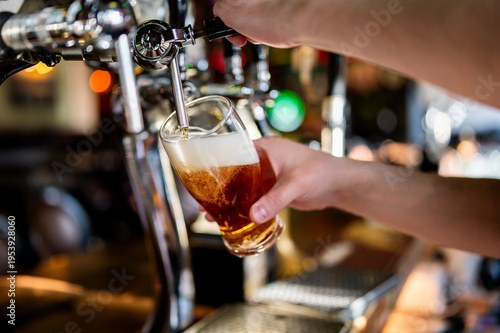 Photography Close-up of a bartender pouring a fresh amber beer from a chrome tap into a glass with foam in a bar