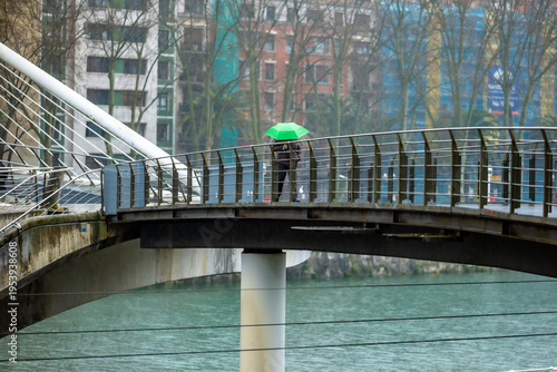 Person with bright green umbrella walking on bridge in rain