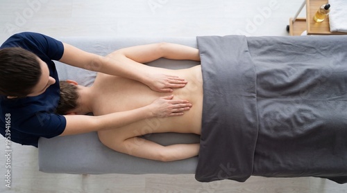 Woman therapist giving back massage to woman patient in spa salon. Professional remedial bodywork session in wellness center. Healthcare treatment for muscle recovery and relaxation.