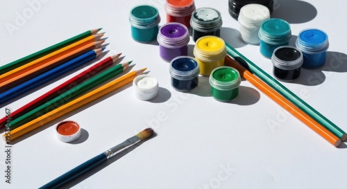 Assorted art supplies on white surface paints, pencils, and a paintbrush