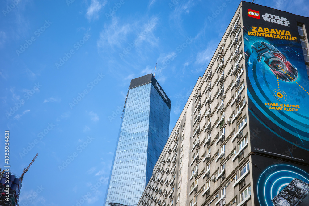 Obraz premium Warsaw, Poland - March 18, 2026: Low-angle view of Warsaw skyscrapers against a blue sky with a Lego Star Wars ad on one building.