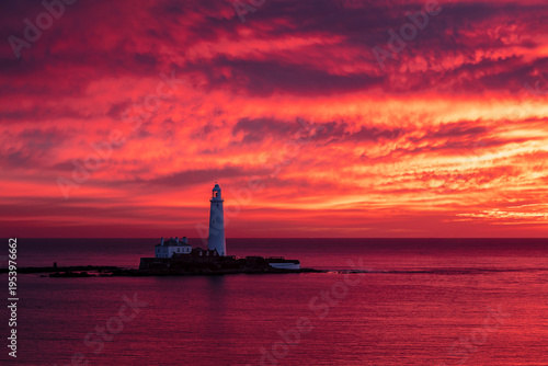 St Marys Lighthouse off the coast of Whitley Bay, North East England.  Bathed in vivid red, blue and purple light from winter sunrise.