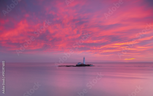 St Marys Lighthouse off the coast of Whitley Bay, North East England.  Bathed in vivid red, blue and purple light from winter sunrise.