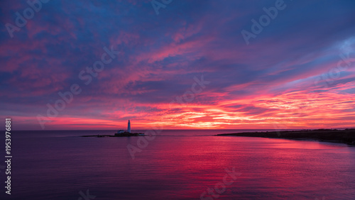 St Marys Lighthouse off the coast of Whitley Bay, North East England.  Bathed in vivid red, blue and purple light from winter sunrise.