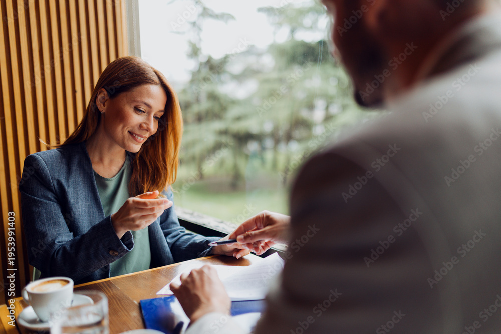 © Novak - Businessman giving a pen to his colleague to sign a document in a cafe