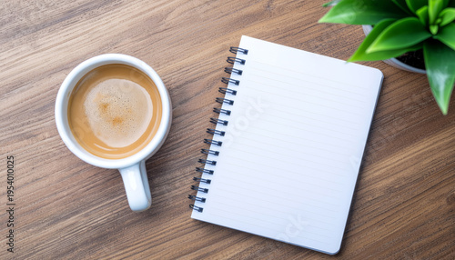 Top view minimalist workspace with white coffee cup, blank spiral notebook and green plant on light wooden desk, calm organized study or work concept, productivity morning routine.