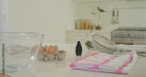 Camera sliding left and back, showing kitchen baking setup: mixing bowl eggs sieve framing station