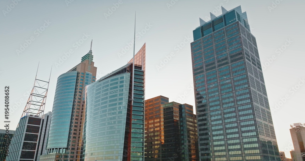 Fototapeta premium Australia, Sydney: Modern glass and steel skyscrapers dominate Sydney skyline, reflecting the warm glow of the sunset sun, creating stunning cityscape architecture background. Drone flight