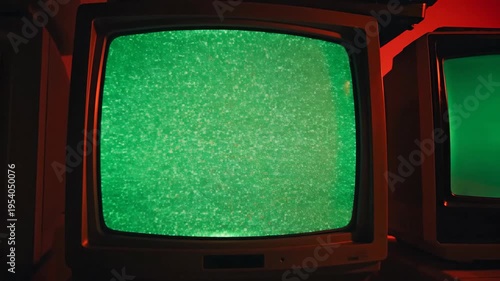 Stack of old televisions with green screens against vibrant red backdrop
