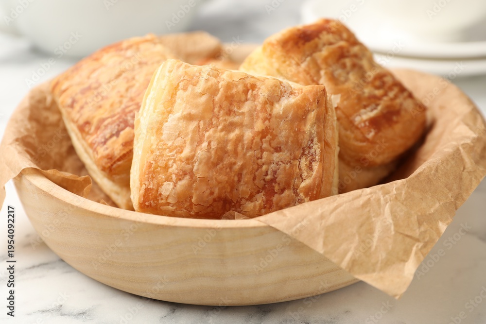 Obraz premium Tasty puff pastries in wooden bowl on white marble table, closeup