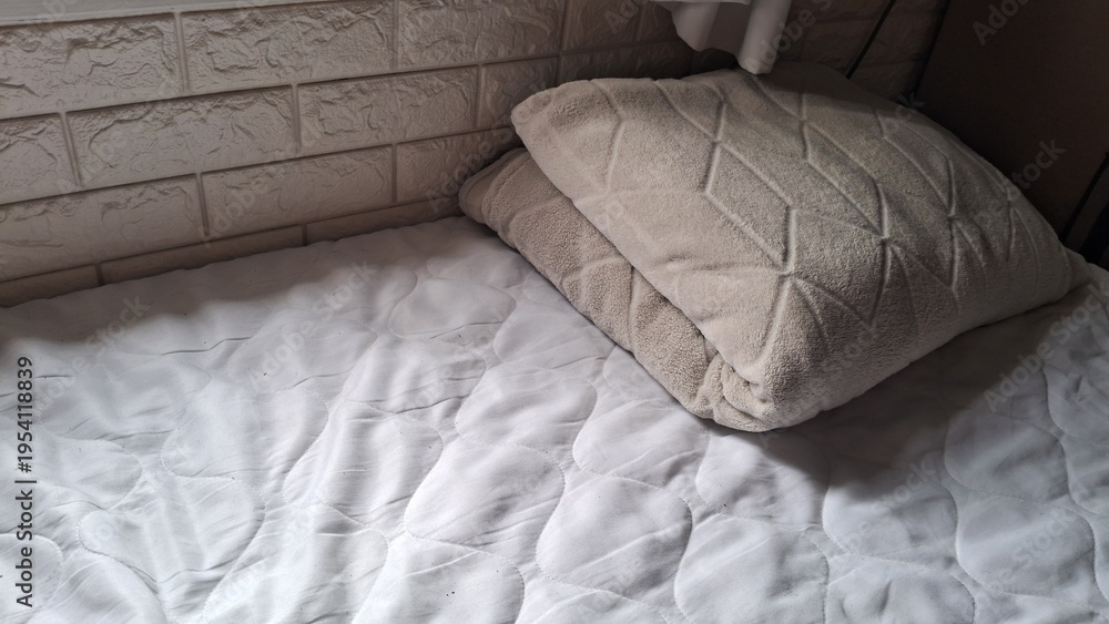Fototapeta premium Comfortable bedroom setup featuring a soft beige textured pillow on a clean white quilted mattress pad.