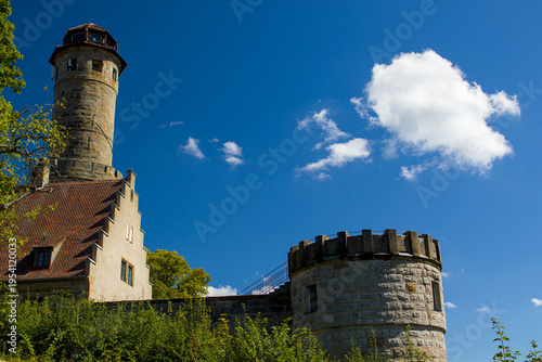 Stone tower rises above an old roof under a deep blue sky. Germany. A round bastion stands near a wall, framed by green trees and sun. Historic architecture in Altenburg shows strength and calm.