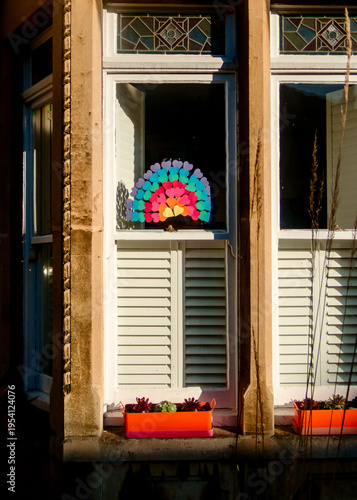 A window with a rainbow made of hearts and two planters with succulents.