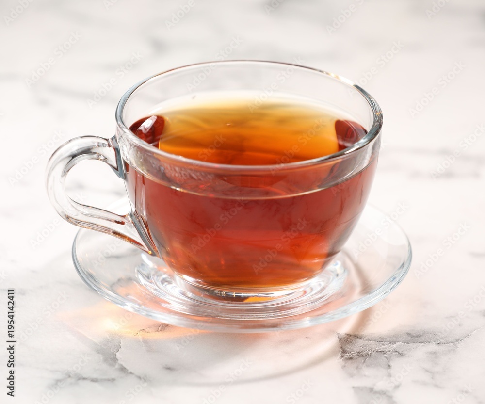 Fototapeta premium Tasty tea in glass cup on white marble table, closeup