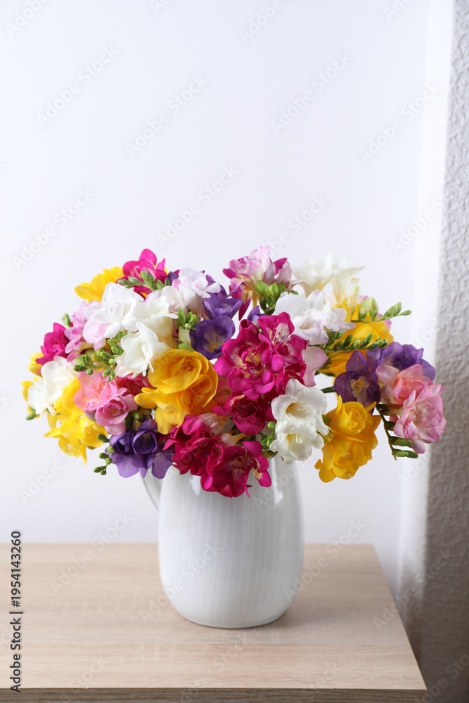 Naklejka premium Beautiful freesia flowers in vase on wooden table near white wall indoors, closeup
