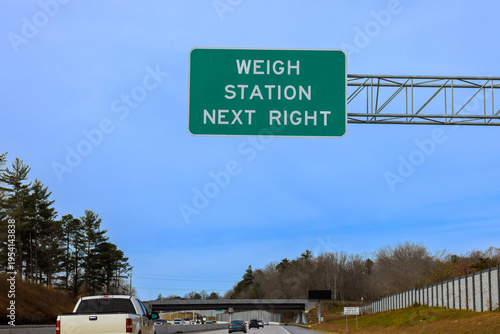 Sign shows direction to weigh station on highway with vehicles on road