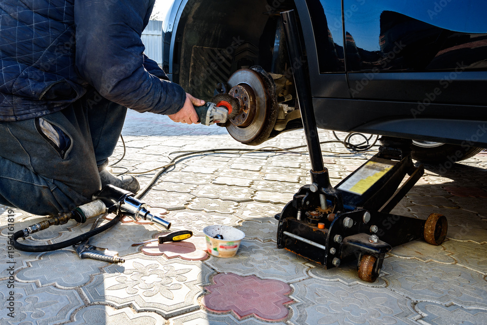 Fototapeta premium A mechanic's hand uses a grinding tool to to clean the disc before changing the wheels outdoor.