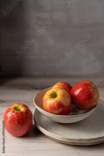 Fresh red apples arranged in a ceramic bowl on a neutral background with soft natural light, minimal composition