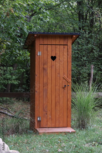 Traditional wooden outhouse toilet with a heart-shaped cutout on the door in a rural setting