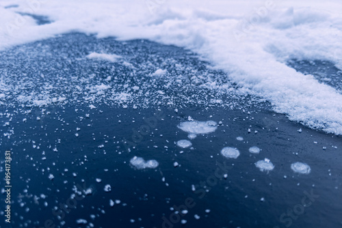 Fotografía Blue frozen pond ice sprinkled with fresh snow crystals and bubbles