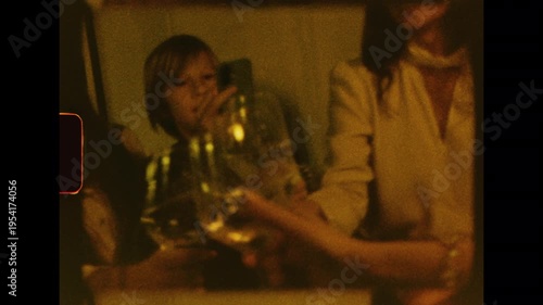 Authentic Super 8mm footage of friends celebrating. A person opens a champagne bottle, and the group joyfully toasts. Warm, grainy, nostalgic home movie style for a retro party scene at night