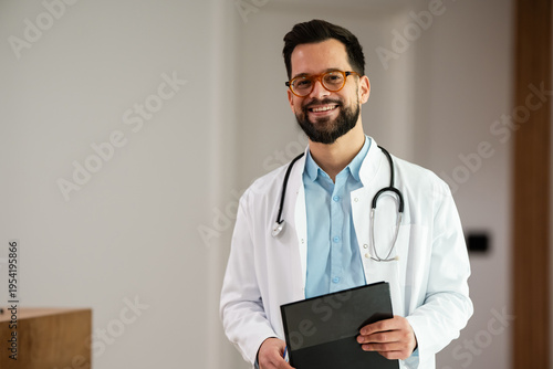 Canvas-taulu Male doctor smiling, holding medical chart in clinic