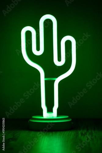 Green neon cactus light lamp glowing in dark interior.