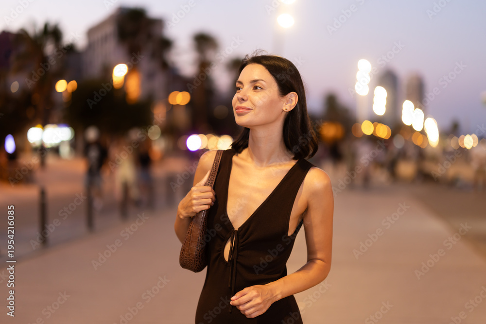 Fototapeta premium Woman walks in vicinity of Citadel park, spend time in public urban space. Atmosphere of relaxation, idleness, entertainment. Electric street lighting..
