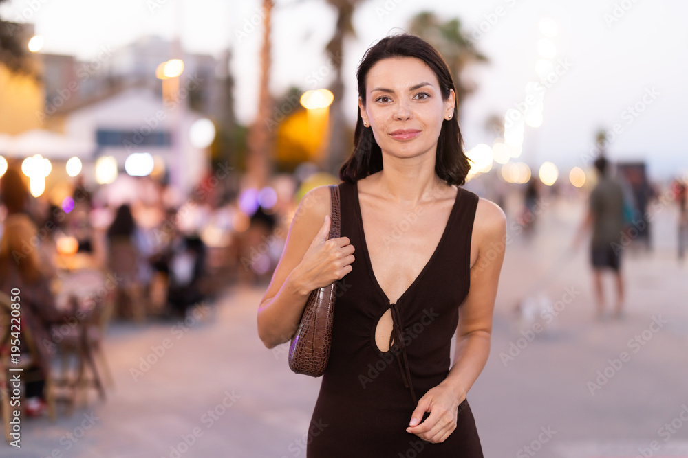Naklejka premium Smiling girl walks around old city district Barceloneta, pedestrian promenade embankment. People are walking by. Person in city, city bustle.