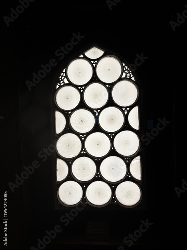 A minimalist architectural window featuring a unique circular geometric pattern illuminated by soft natural light. The symmetrical design creates a visually striking abstract composition, blending mod