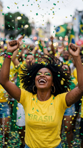 Uma mulher negra, torcedora do time do Brasil, usando camiseta amarela vibrando com os punhos cerrados pra cima.