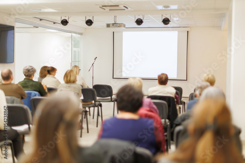 Audience attends a presentation in a meeting room with a projector screen at the front