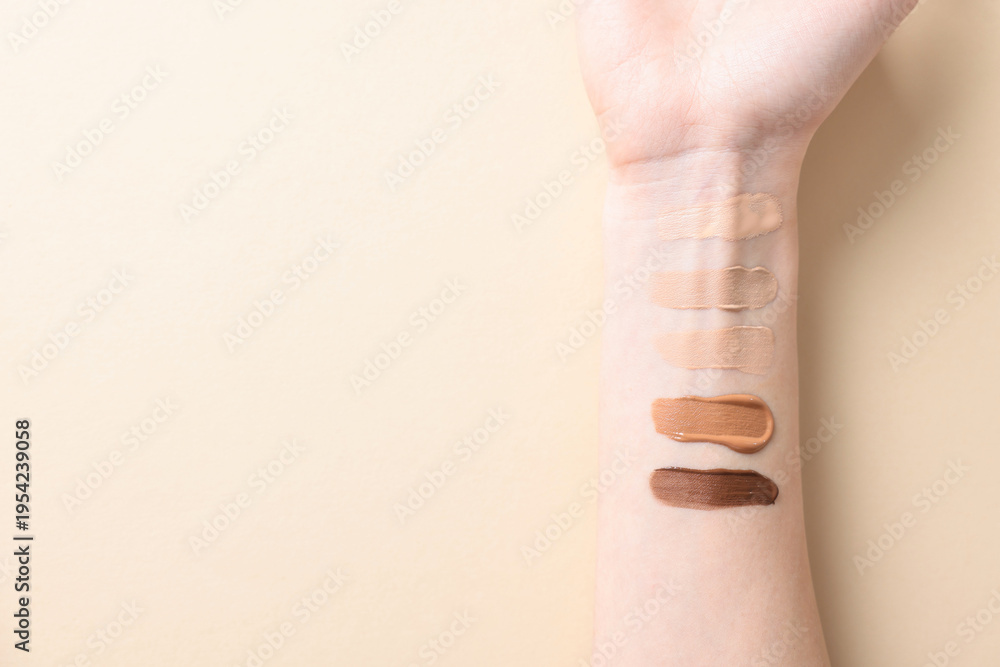 Fototapeta premium Woman with different shades of foundation on her arm against beige background, top view. Space for text