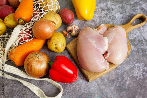 Fresh raw chicken and assorted vegetables on a grey counter for healthy cooking