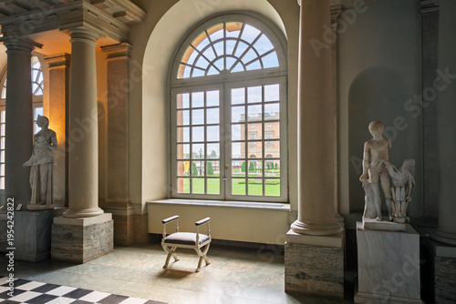 Photography A solitary chair sits in front of an arched window with a view of the Logården, the garden of the Royal Palace, from inside the hall of antiquities in Stockholm, Sweden