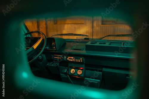 Vintage van interior viewed from the back seats, showing a simple dashboard, steering wheel, and manual gear shift. Warm exterior light contrasts with cool teal cabin tones, creating a retro, moody