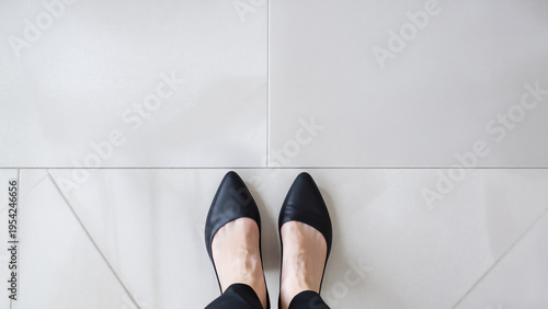 白い床に立つ女性の足元と黒いパンプスのミニマル構図