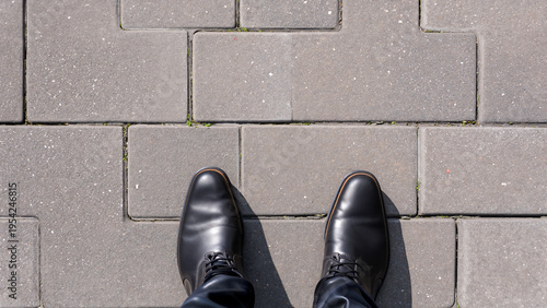 足元視点で見る石畳の歩道と黒い革靴のビジネスイメージ
