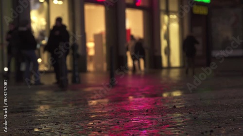 Blurred silhouettes of pedestrians in Night City Street with Neon Reflections on Wet Cobblestones