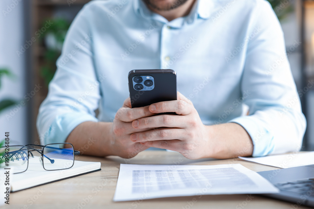 Fototapeta premium Man using modern smartphone at wooden desk in office, closeup