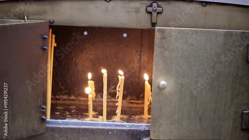 A candle burns softly, casting warm light through the gap of heavy metal doors
