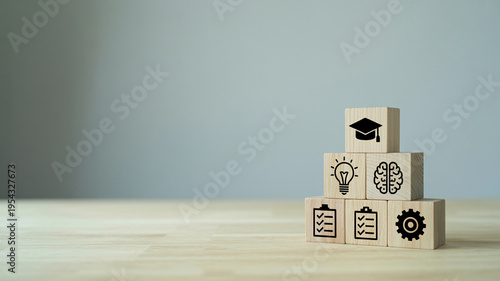 A stack of wooden blocks with educational icons on a light wood table against a gray background