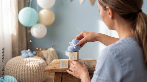 Expectant white mother placing a blue knitted baby bootie on wooden blocks spelling baby in a pastel nursery. Caregiver arranging newborn booties and wooden blocks on a rustic table for newborn decor