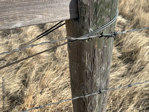 Close up of weathered wooden fence post with barbed wire in rural prairie farmland setting