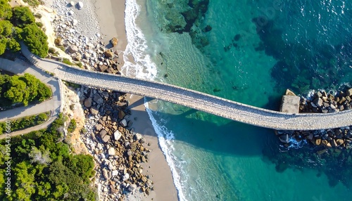 Wallpaper Mural Aerial view captures a stone bridge extending over vibrant turquoise water, leading to a sandy shore and rocky coastline. Lush green trees flank the path Torontodigital.ca