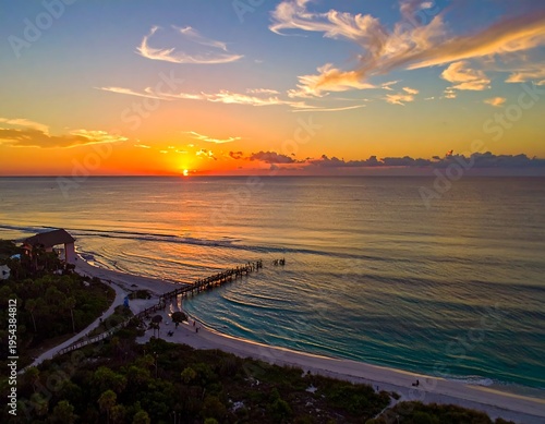 Wallpaper Mural Aerial view of a beach at sunrise. The sky blazes with orange and blue hues reflecting on the ocean's surface. A long pier extends into the sea Torontodigital.ca