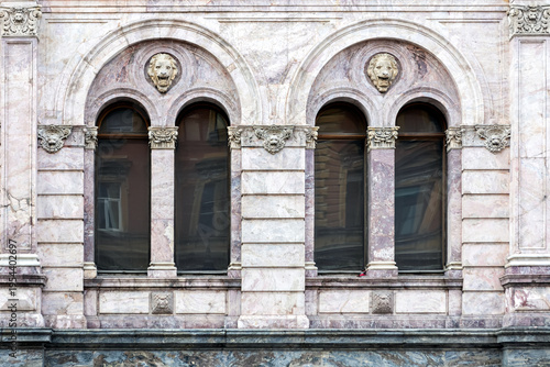 Two arched windows with a column and a bas-relief on a wall made of marble slabs. From the Windows of the world series.