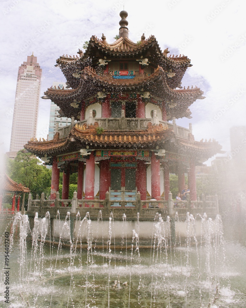 Fototapeta premium Description: Ornate traditional Chinese temple pavilion with intricate roof details and symmetrical stone stairways, surrounded by greenery under an overcast sky